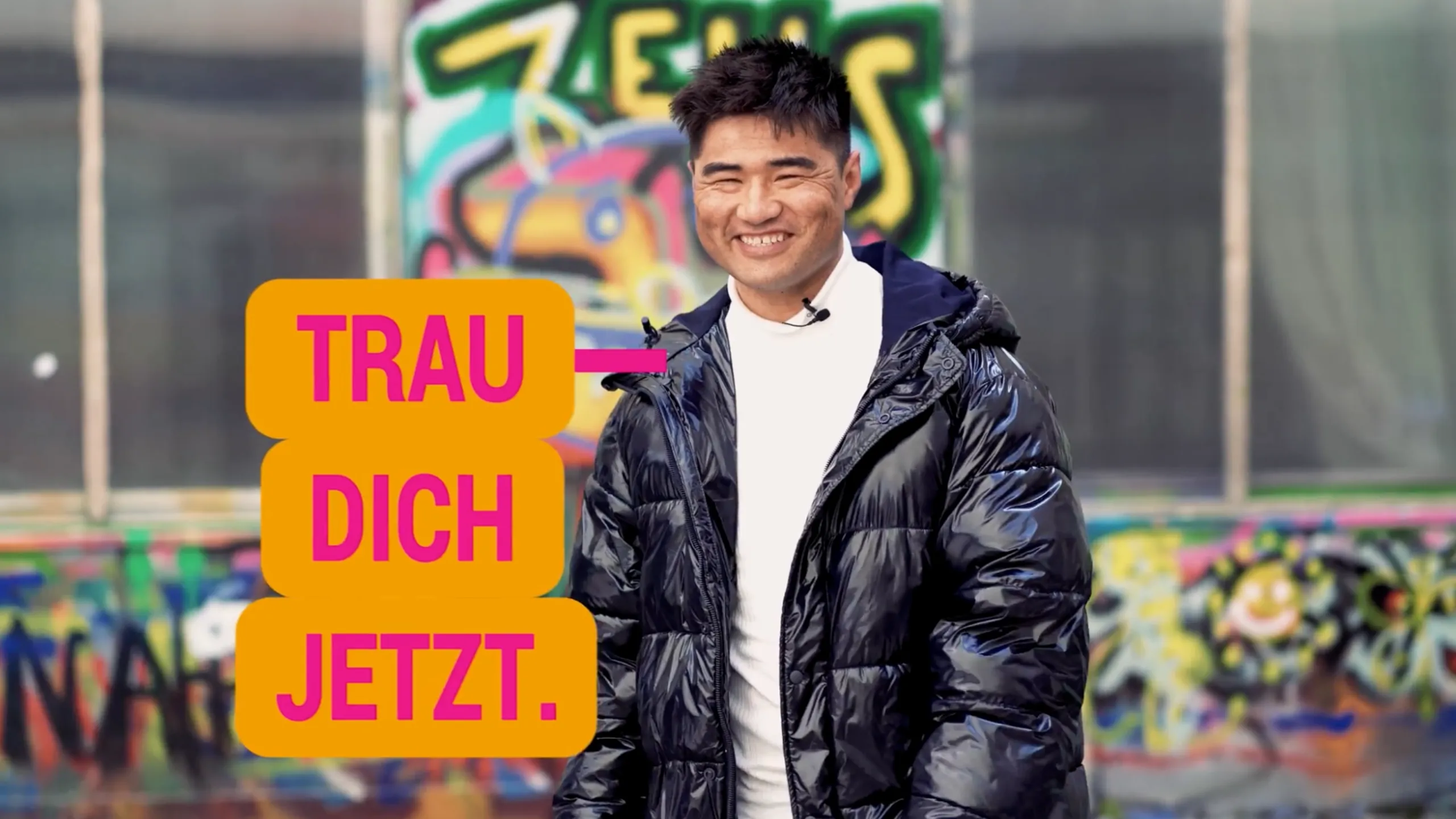 Mann vor Graffiti-Wand mit Kampagnenbotschaft „Trau dich jetzt“ zur Mitarbeitergewinnung in der Pflege