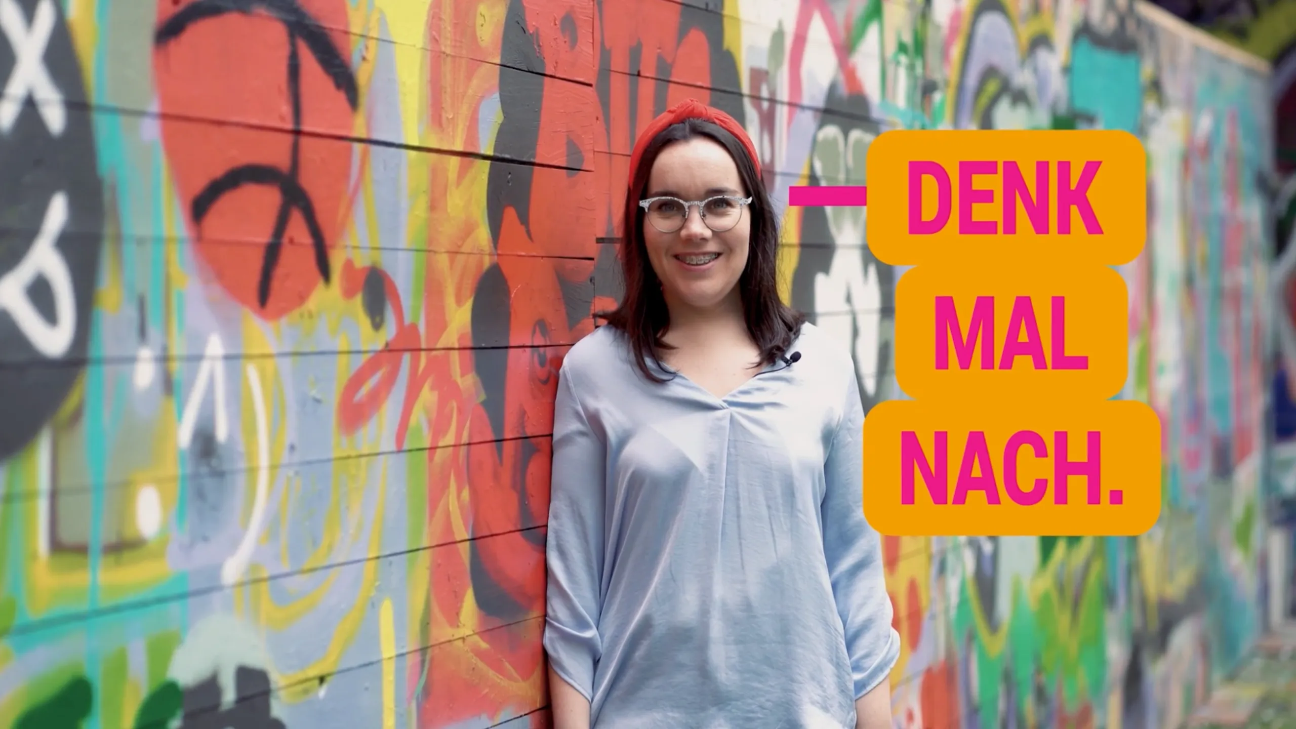 Frau mit Brille vor urbaner Graffiti-Kulisse mit Botschaft „Denk mal nach“ – Pflege Recruiting-Kampagne