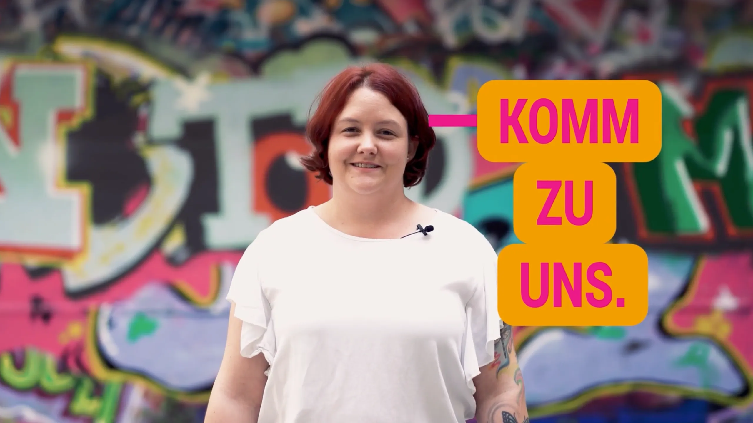 Frau vor Graffiti-Hintergrund mit Schriftzug „Komm zu uns“ – Mitarbeitergewinnung im Pflegebereich