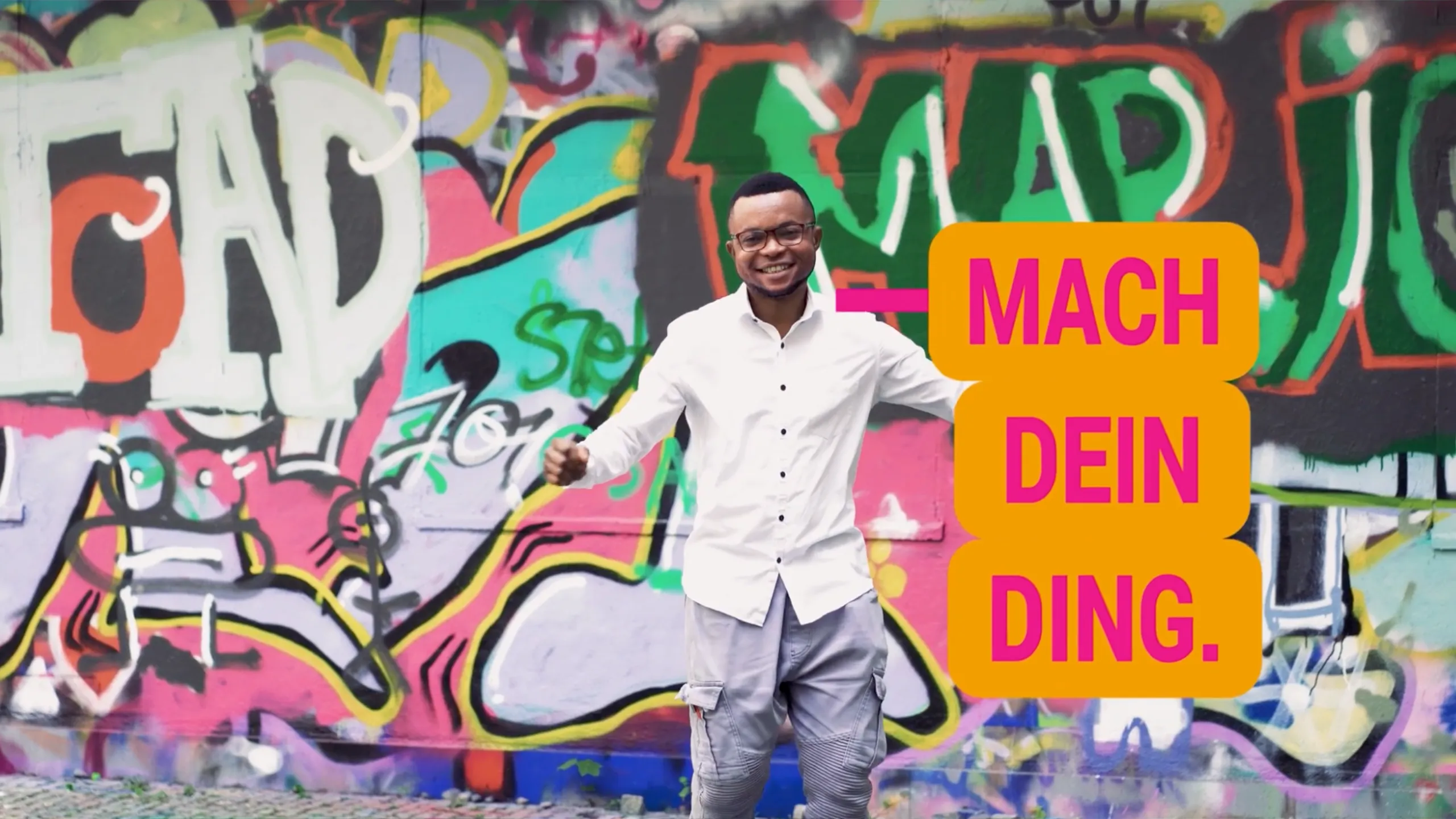 Mann vor farbiger Graffiti-Wand mit Botschaft „Mach dein Ding“ – Recruiting-Kampagne Pflege